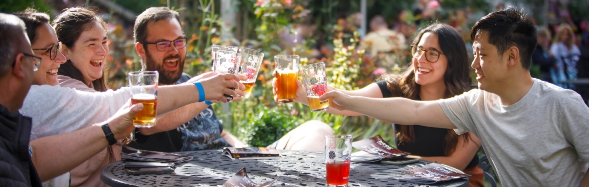 A group of people saying cheers and clinking glasses in the garden at the Merchant Adventurers' Charity Beer Festival.