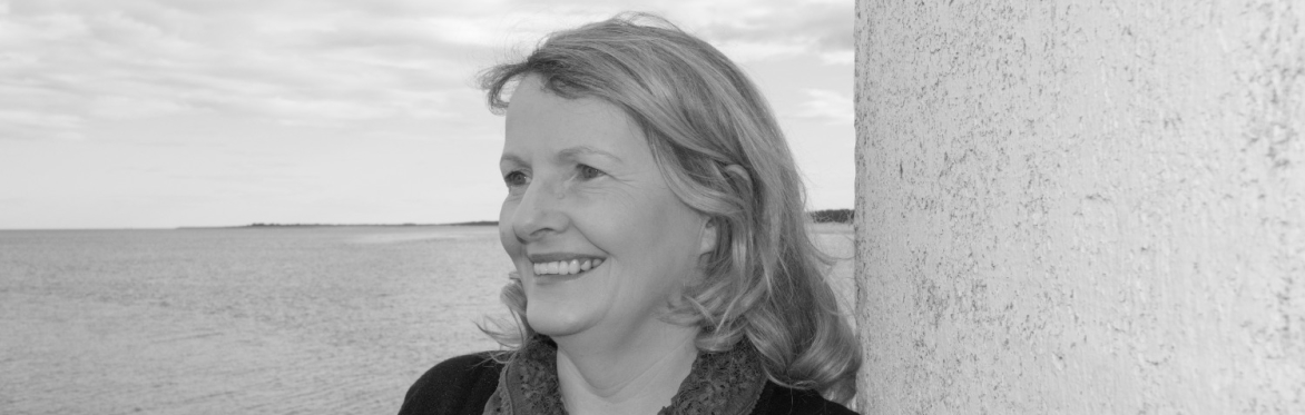 A black and white picture of a head and shoulder pic of Helen Forbes leaning against a wall overlooking a seaview