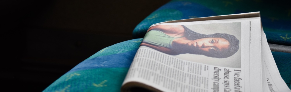 A photograph of a folded up newspaper on the seat of a train with a black woman wearing a green top as the article photo and the headline of the article obscured.