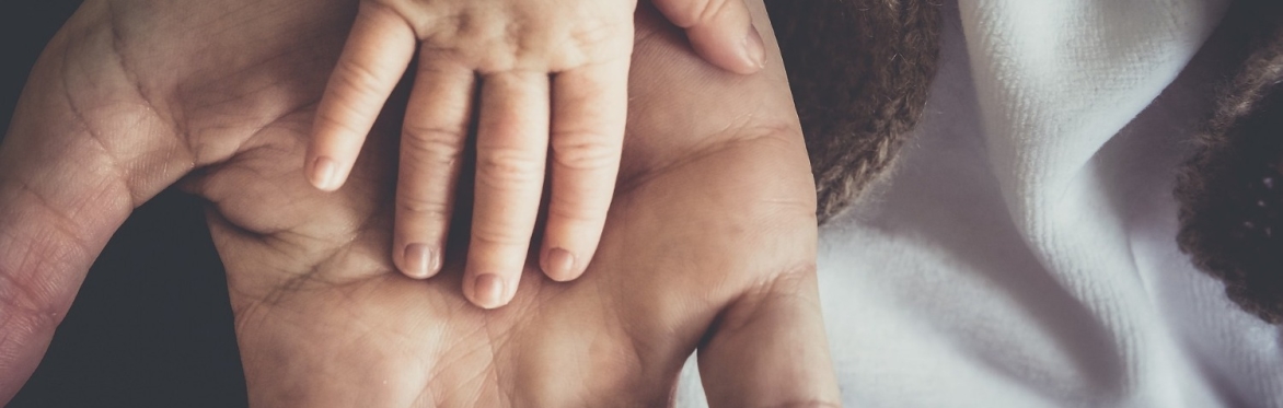 A small child's hand rests, palm down, on top of an adult hand which is palm up
