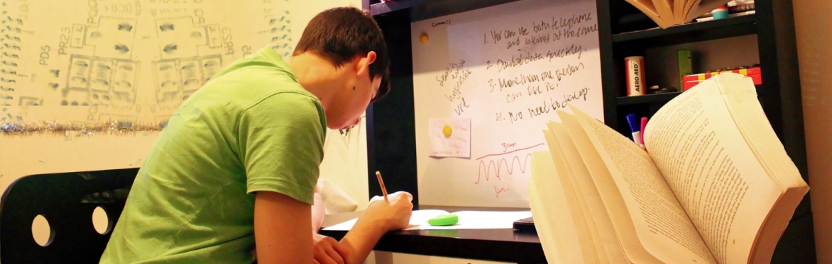 Teenage boy sitting writing at desk surrounded by notes