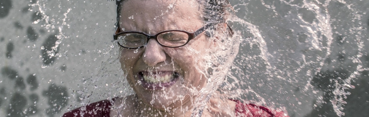 A woman has her face splashed with a large amount of water, she seems happy enough