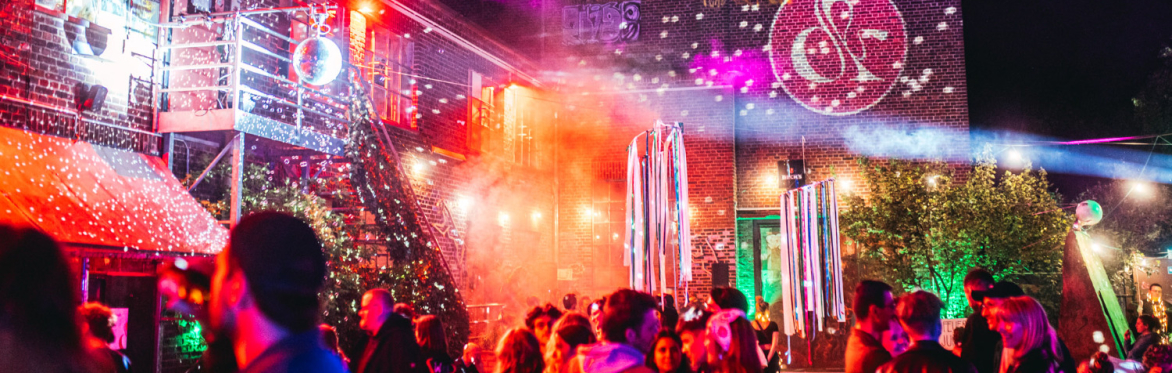 Das Bild zeigt das Luft&Laune Festival. einer Mischung aus farbigem Licht, Nebeleffekten und einer ausgelassenen Menge. Graffiti und Projektionen.Discokugeln,  kreativen, alternativen Events.