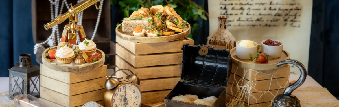 An pirate themed afternoon tea including scones in a treasure chest, an alarm clock and the food presented on crates with fish nets.