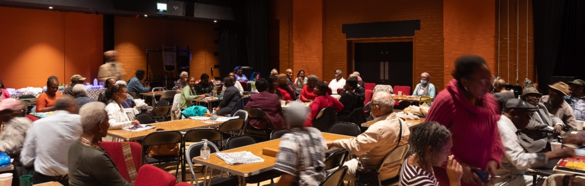 A group of people are gathered at tables at a community event in the Tramshed Theatre