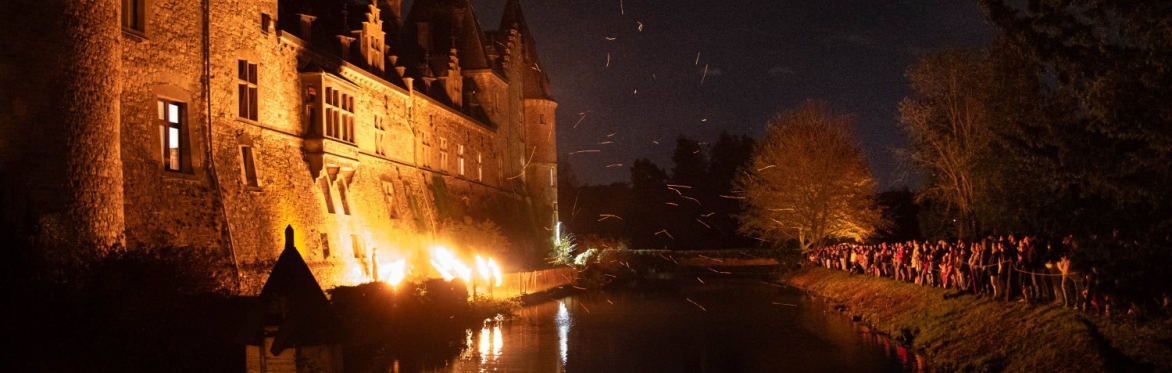 Photo : façade sud illuminée, jongleurs, douves et public sur la berge en face