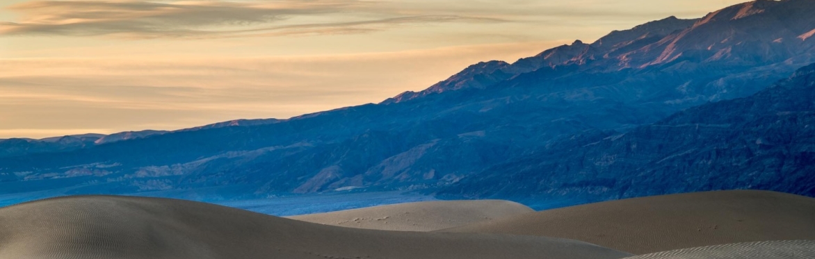 Sand dunes leading to mountains under a peach sky