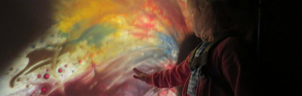 A young child reaches out their hand to touch a projection of splashy colours