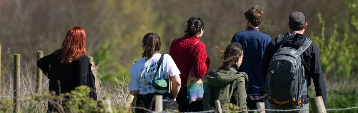 A group of people walking together across the boundary of the University of Sussex campus