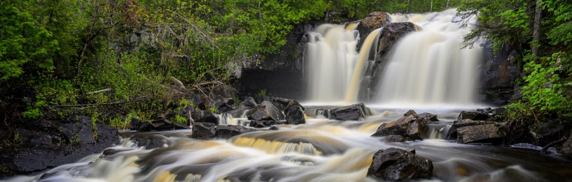A photo of a waterfall and small stream surrounded by green trees.