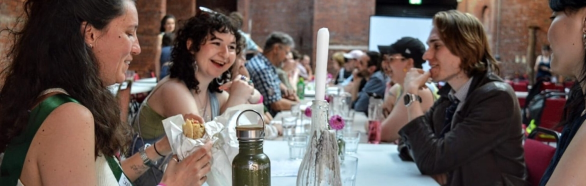 a group of smiling people sitting at a long table with food and candles and flowers