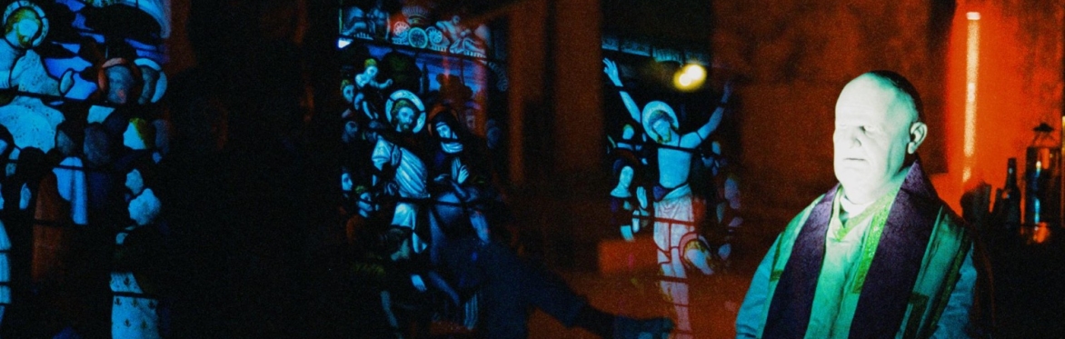 A double exposed photograph, depicting the artist dressed as a priest, overlaid with stained glass windows.