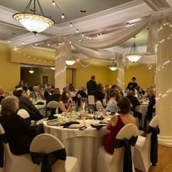 A large, grand ballroom event with string lights around columns and well-dressed guest seated at white linen tables.