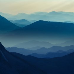 Snow-dusted rugged mountain peak under a cloudy sky, with dramatic dark rock formations. The scene conveys a sense of solitude and awe.