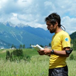 Primo piano dell' Accompagnatore di Media Montagna Luca Stefenelli mentre legge da un libro durante un'escursione. Si trova in uno spiano erboso in montagna