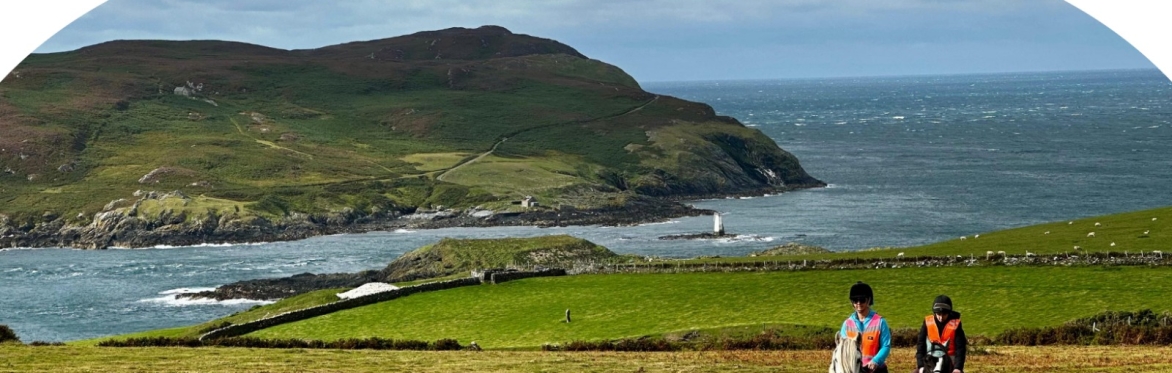 Two riders in high-vis on horses with the Sound and the Calf of Man in the background.