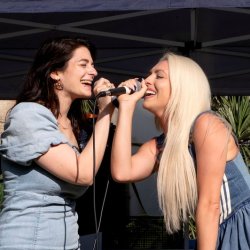 Two young women sing into a microphone at an outdoor karaoke event.