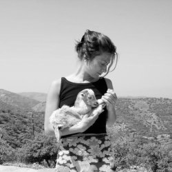 Phoebe Giannisi holds a baby goat, in front of a hilly landscape.