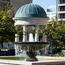 Kogan Plaza on GW's Foggy Bottom Campus, with a fountain in the foreground and a building with a rounded roof in the background