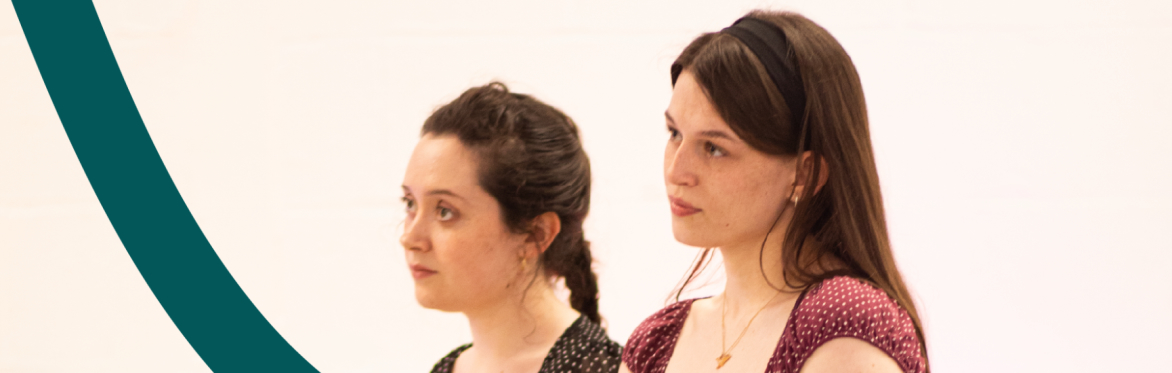 Two young performers sit on chairs with scripts resting on their laps.