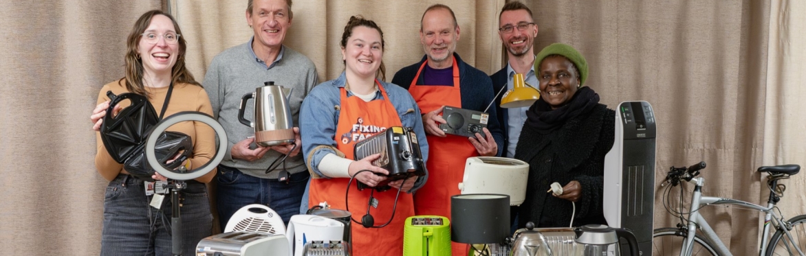 A group of people holding electrical appliances that have been fixed at the Fixing Factory