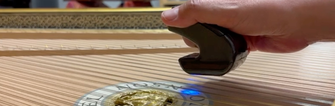 Hand holding an electronic bow over the strings of a harpsichord