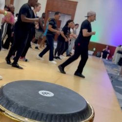 Dancers practicing salsa with a conga drum in the foreground