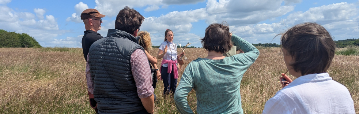 Jane Ibrahim talks to a group of people standing in a field, holding a deer skull