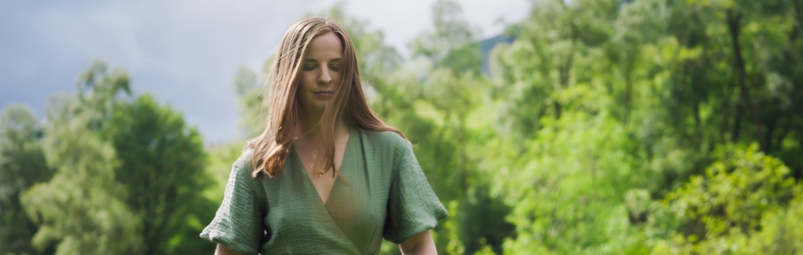 Beth in the countryside looking down and wearing a green dress