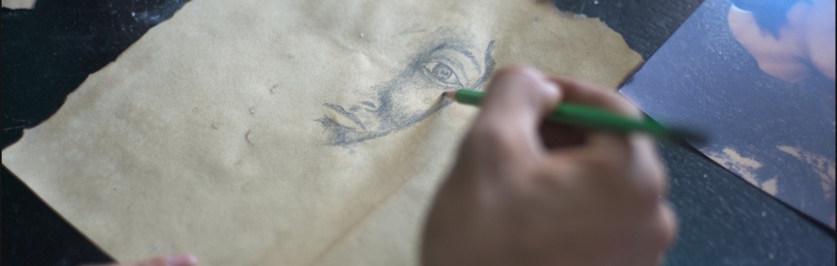 Film still featuring a close up of a hand drawing a face with a pencil