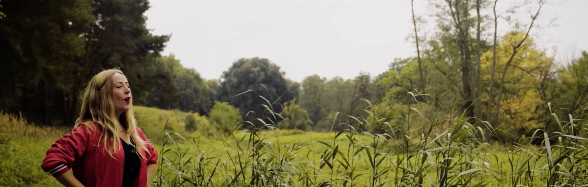 Woman yodels across green field surrounded by forest