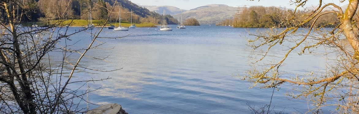 An image of Windermere under a blue sky with a few boats on the lake.