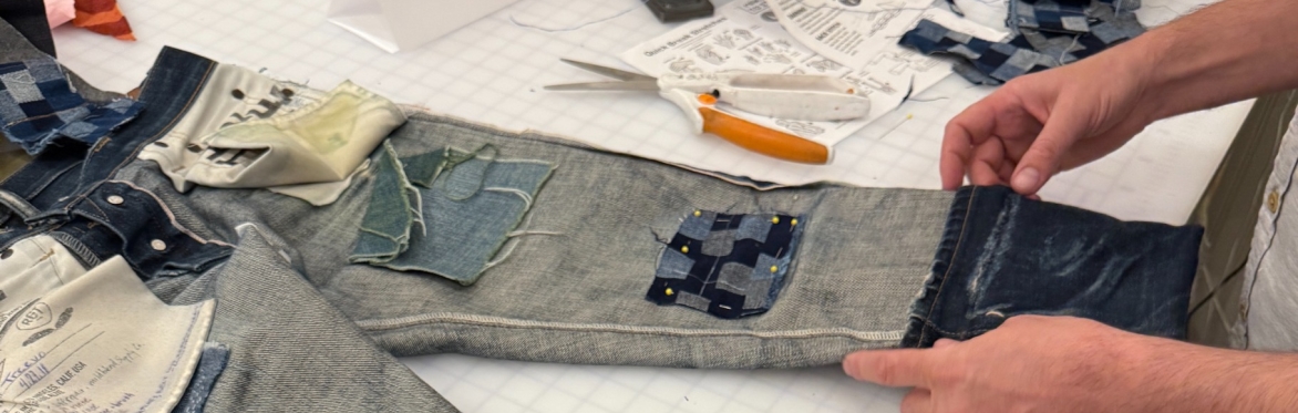 Hands fold the hem on an inside-out, patched pair of jeans.