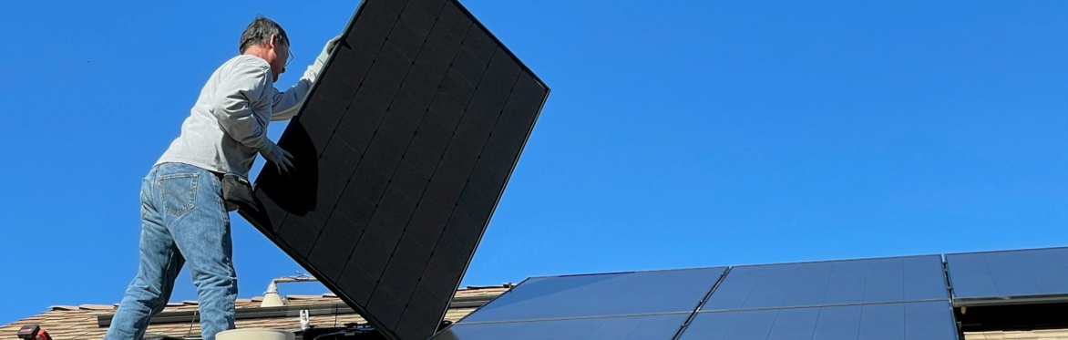 A man installing solar panels on a roof with blue sky behind