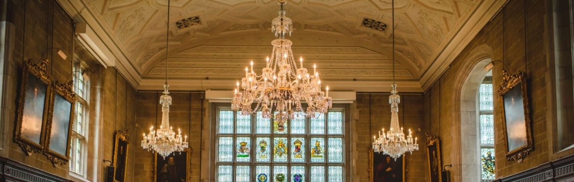 A Tudor style banqueting Hall. Wood panelled walls, colourful heraldic stained glass, ornate chandeliers and historic portraits.