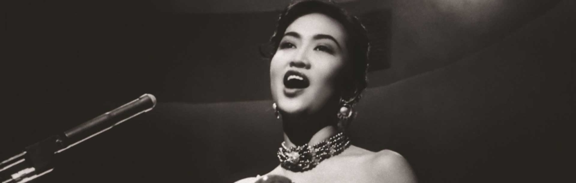 A monochrome image of a woman singing into a microphone, capturing her expressive performance.