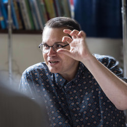 Composer Paul Mealor gestures expressively as he leads a masterclass, speaking with a participant seated in the foreground.