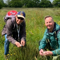 Image of two people crouching down in a sunny meadow.