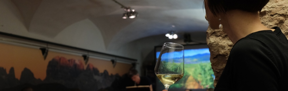 In primo piano, sul lato destro, è presente il profilo di una donna che tiene un calice di vino bianco. Nella parte sinistra si trovano delle persone sedute. Tutti stanno ascoltando