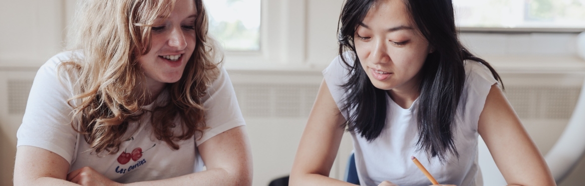 Two young ladies looking at a textbook together in a classroom.
