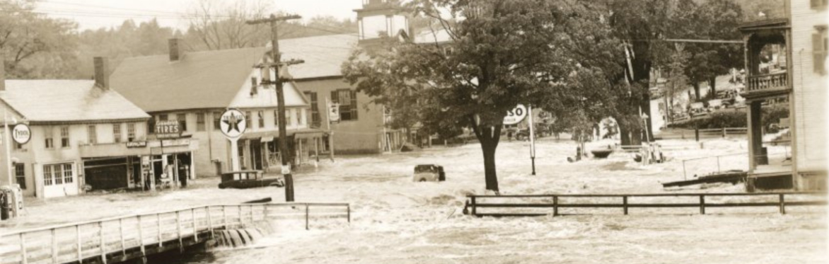 black and white photo showing a heavily flooded street with 1930s era cars in the water. The water is above the height of the tires.