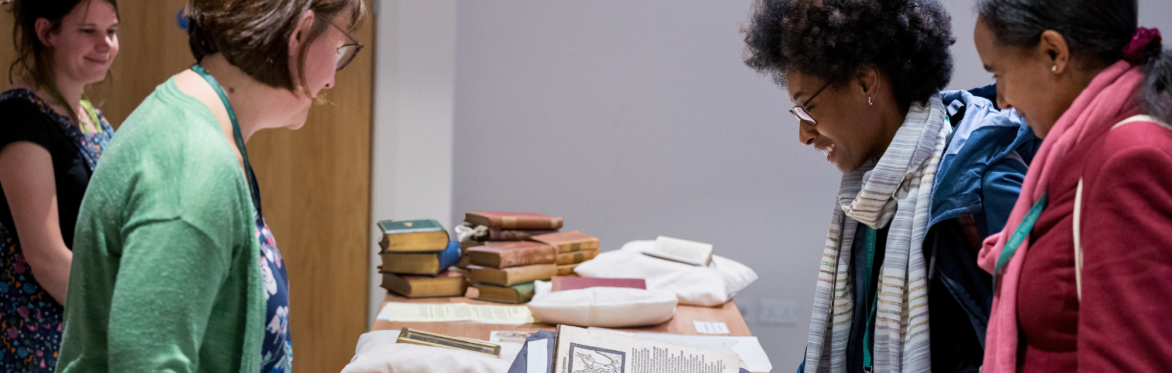 People stood either side of a table filled with open books resting on cushions.