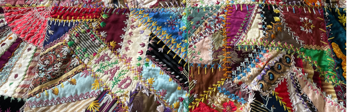 Close up view of a colorful crazy quilt with a variety of fabrics stitched together using colorful embroidery in various stitching patterns.