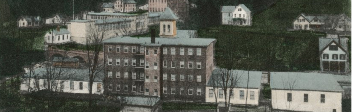 Colorized early 20th century postcard showing brick and wooden mill buildings and a few houses.