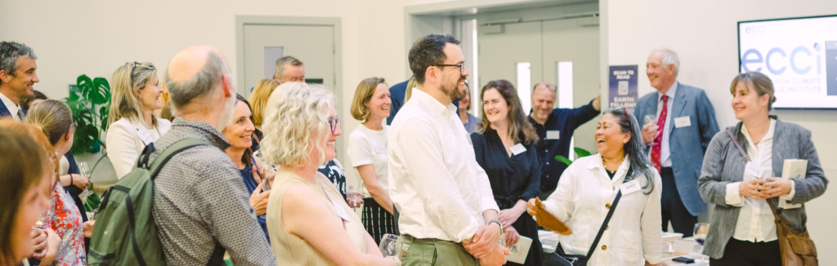 A group of people are drinking and listening to a speaker and smiling and chatting
