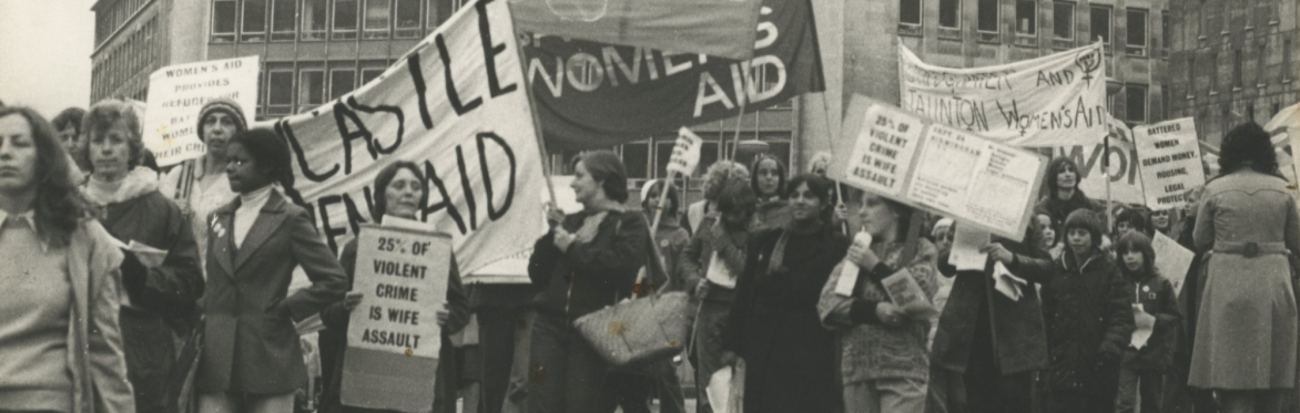 A black and white photo of women and children marching down the street with Women's Aid banners