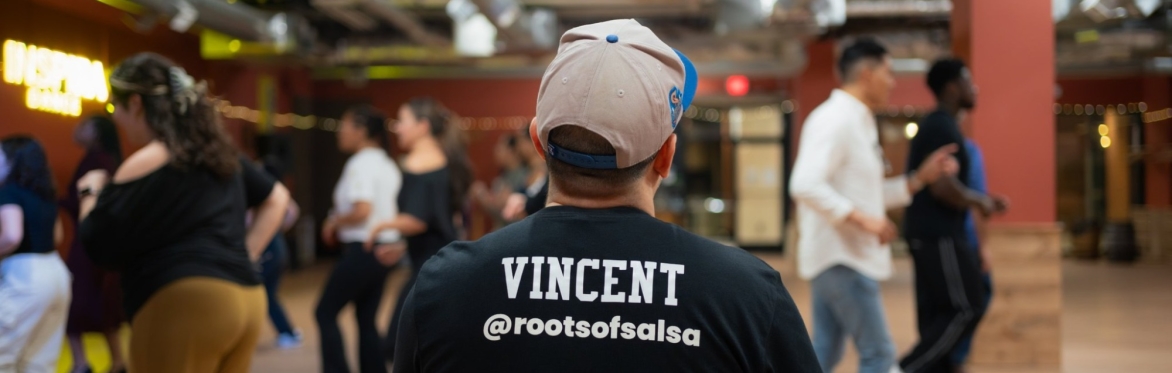 Beginner salsa dancers practicing across the floor at Inspira Dance in Ballston, with Vincent of Roots of Salsa watching from the front.