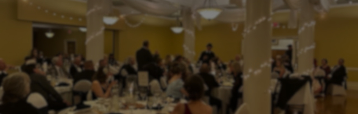 A large, grand ballroom event with string lights around columns and well-dressed guest seated at white linen tables.