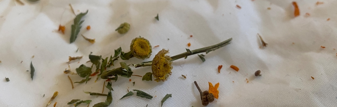 A stack of four folded bandanas each speckled with different colours with a sprig of dried tansy on top.