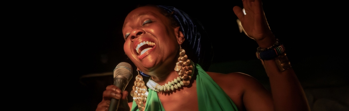 Black woman wearing headscarf, big jewellery and holding microphone